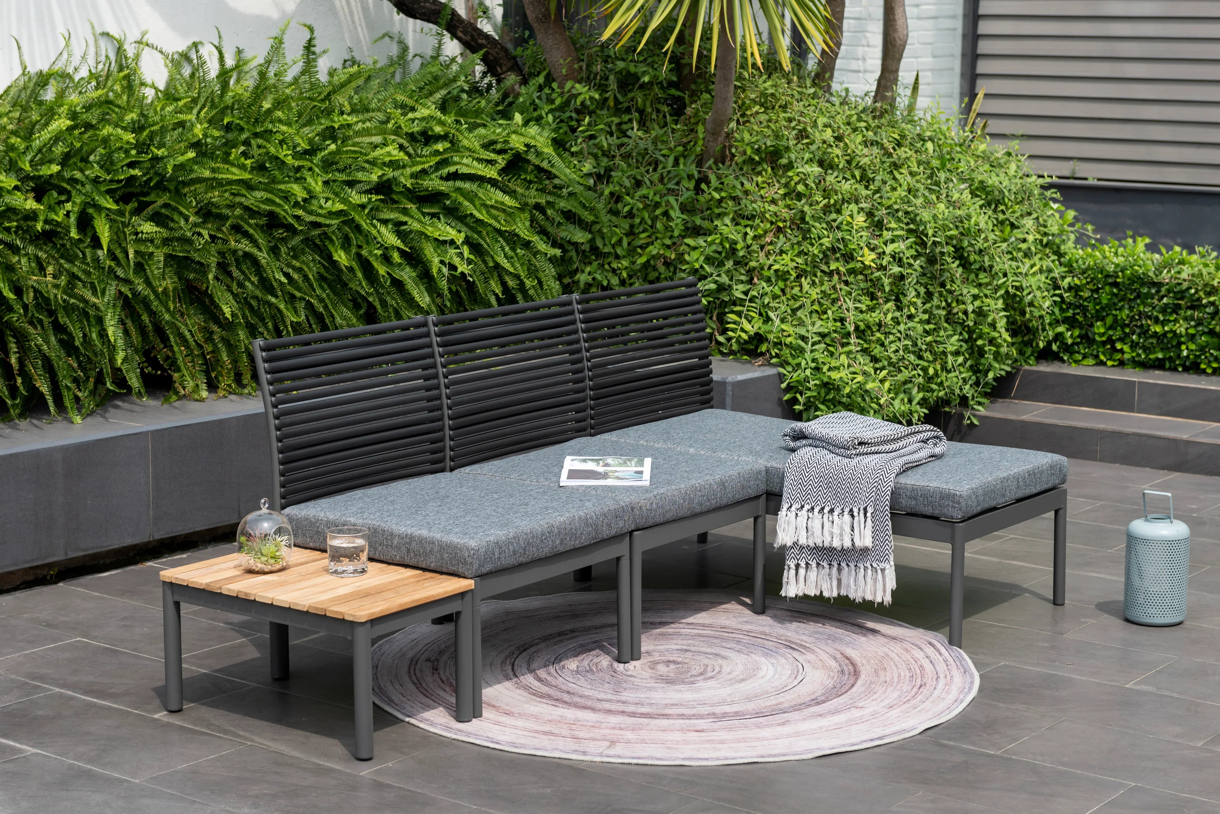 Modern outdoor sofa set with gray cushions, black frame, side table and patio rug on tiled terrace