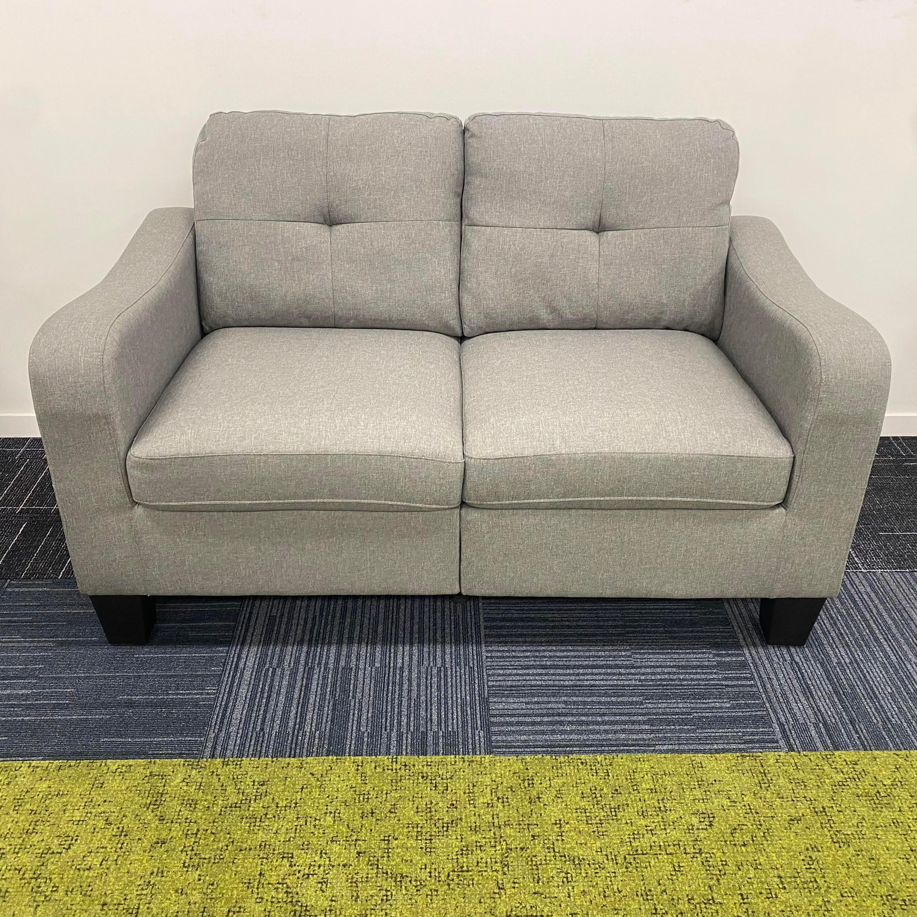 Modern grey fabric two-seater sofa with tufted cushions on patterned carpet