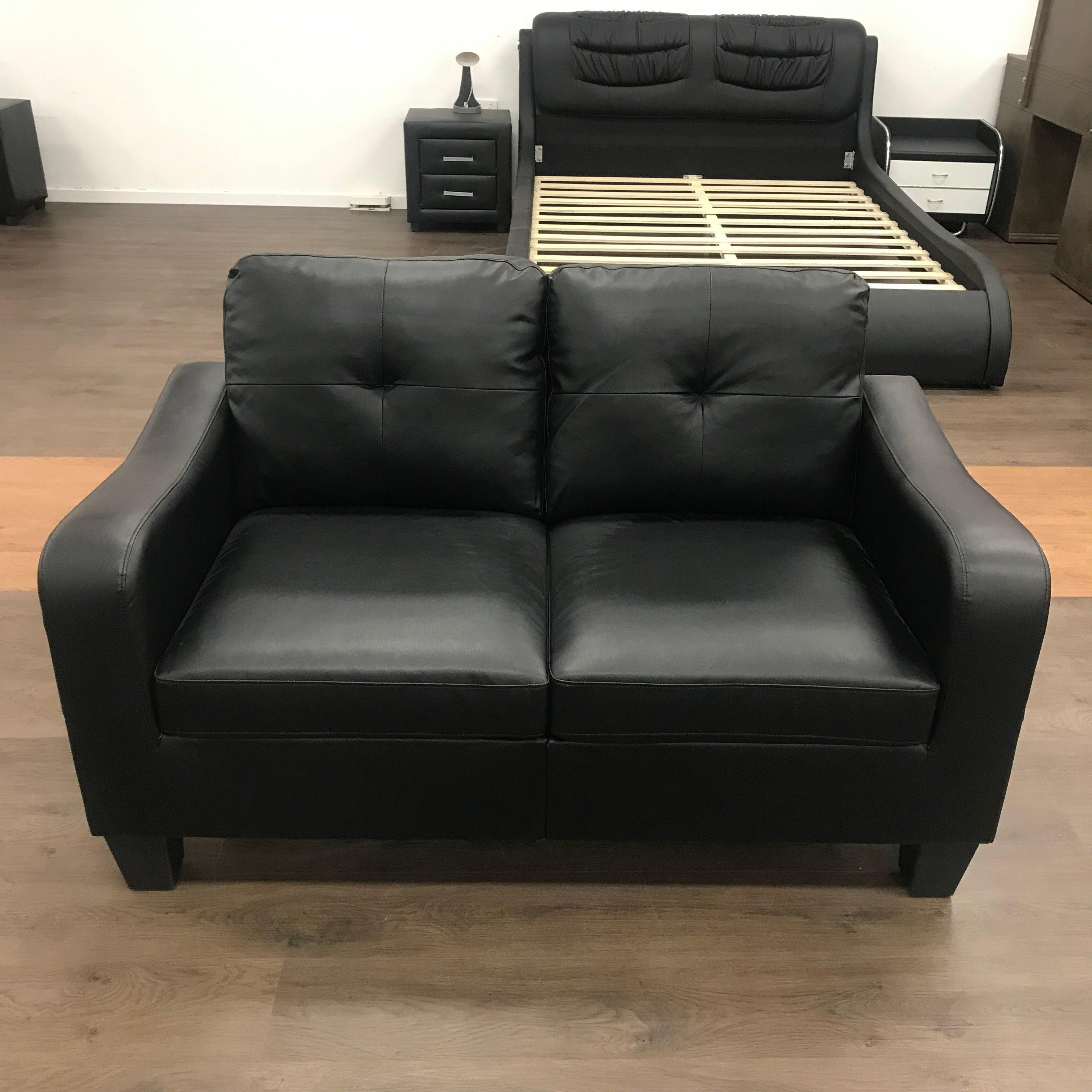 Black PU leather loveseat sofa on wooden floor with bed frame and bedside tables in background