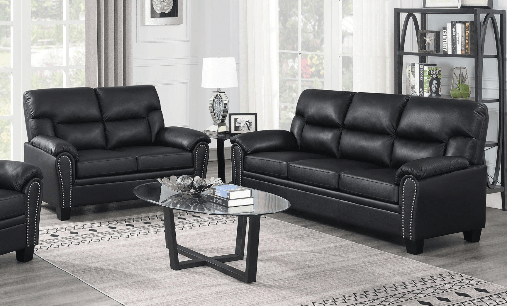 Modern living room with black leather sofa set, studded arms, and glass coffee table on rug.