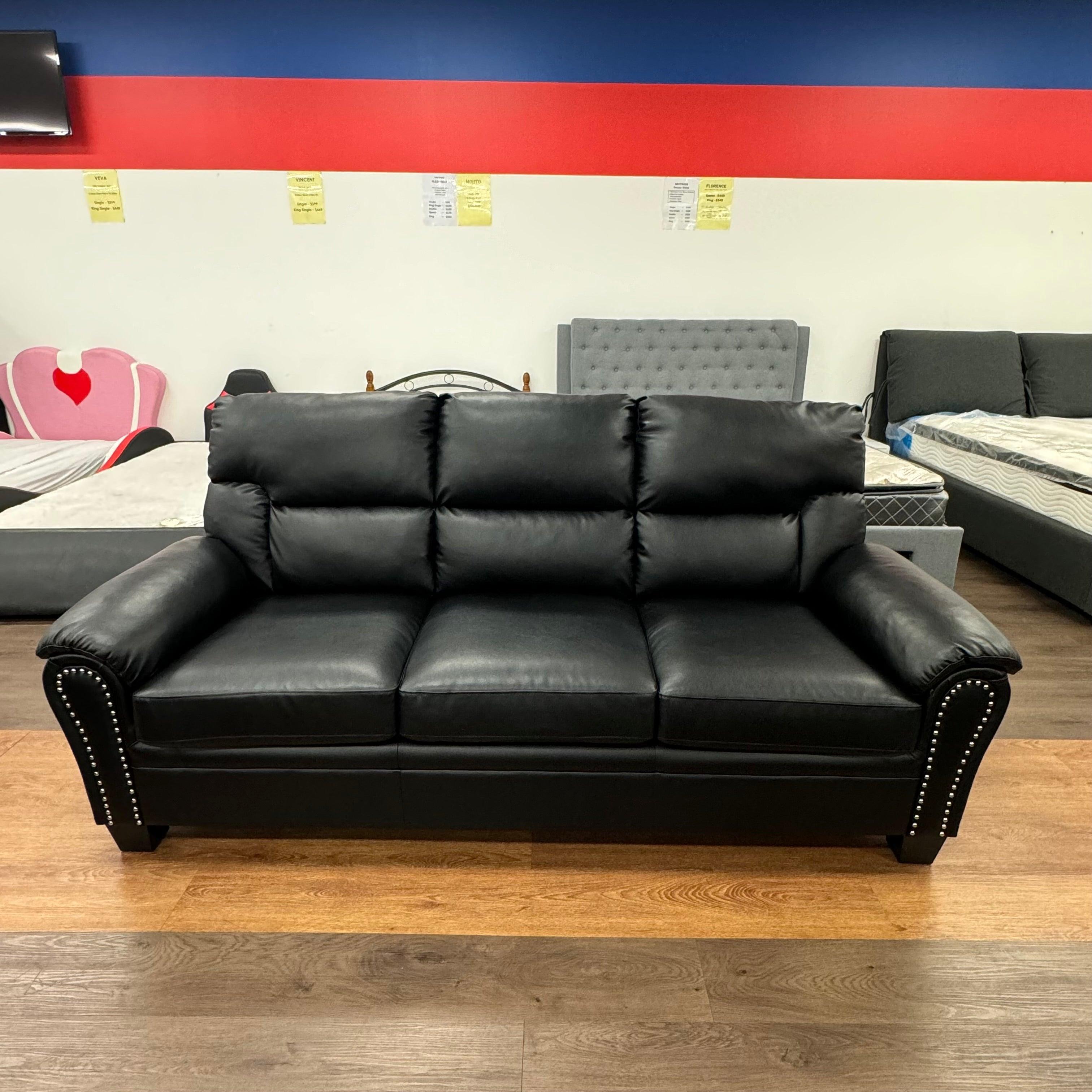 Black leather three-seater sofa with studded arms in furniture showroom setting