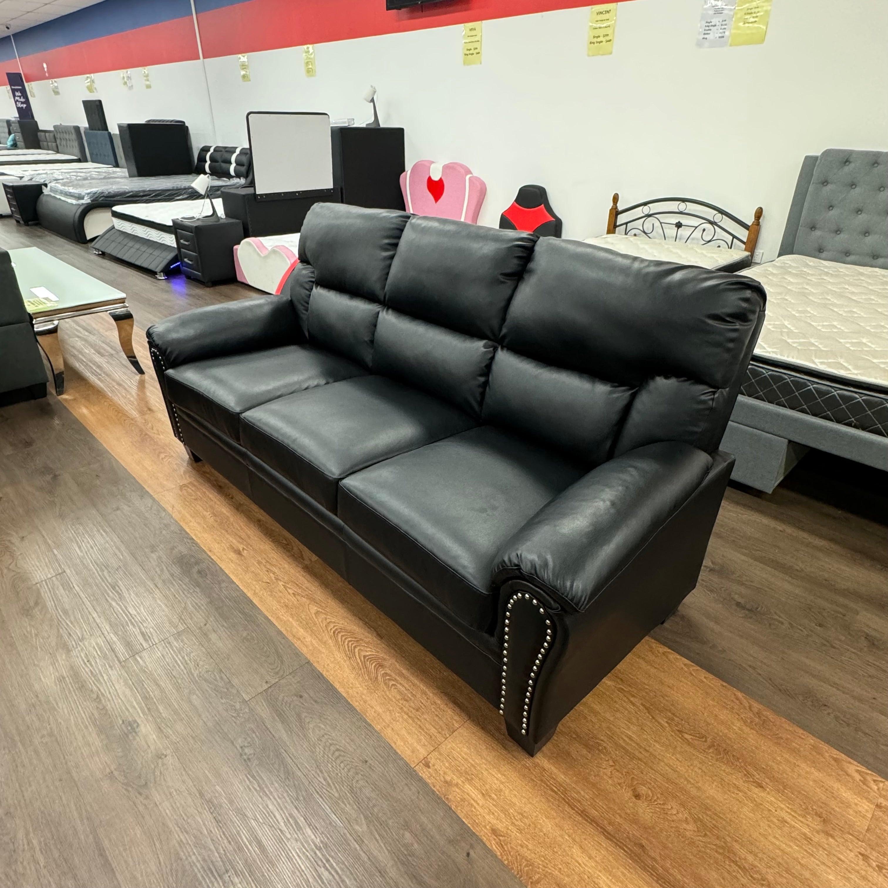 Black leather three-seater sofa with studded arms in furniture showroom with beds