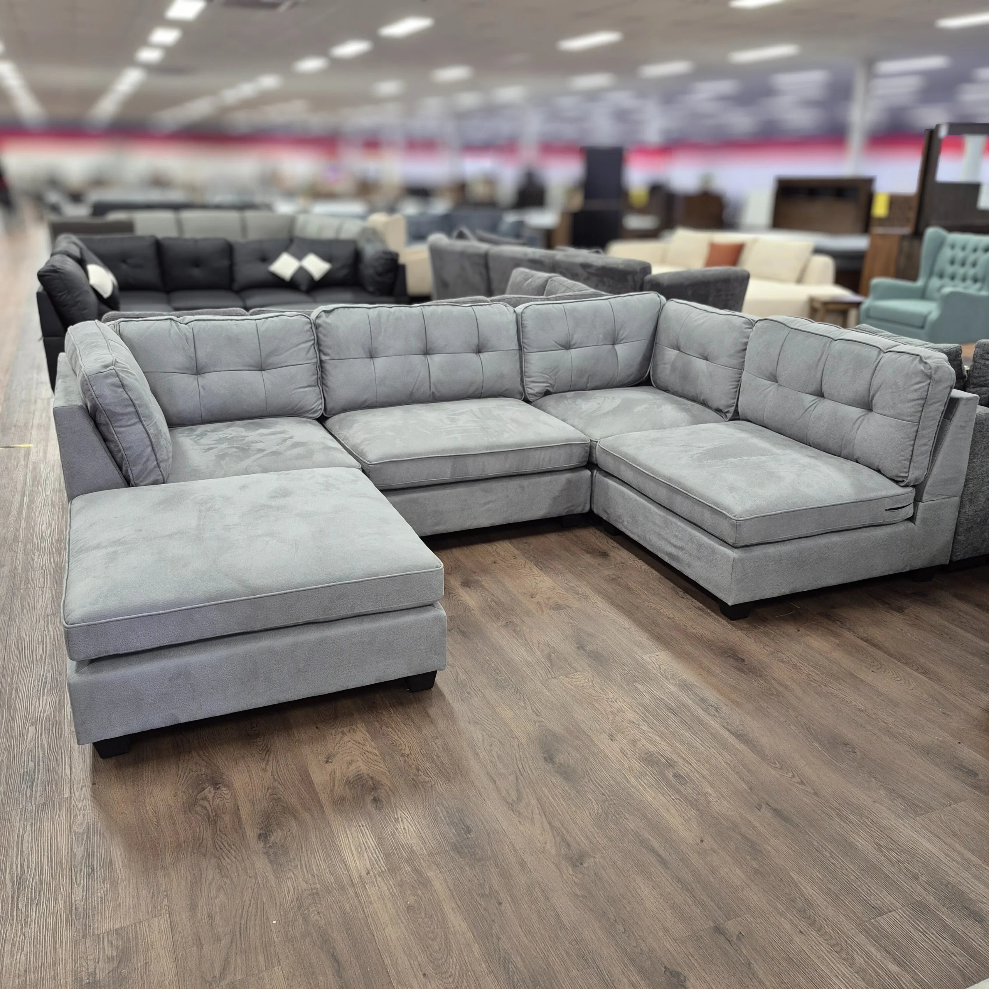 Light grey U-shaped sectional sofa with tufted cushions in a furniture showroom