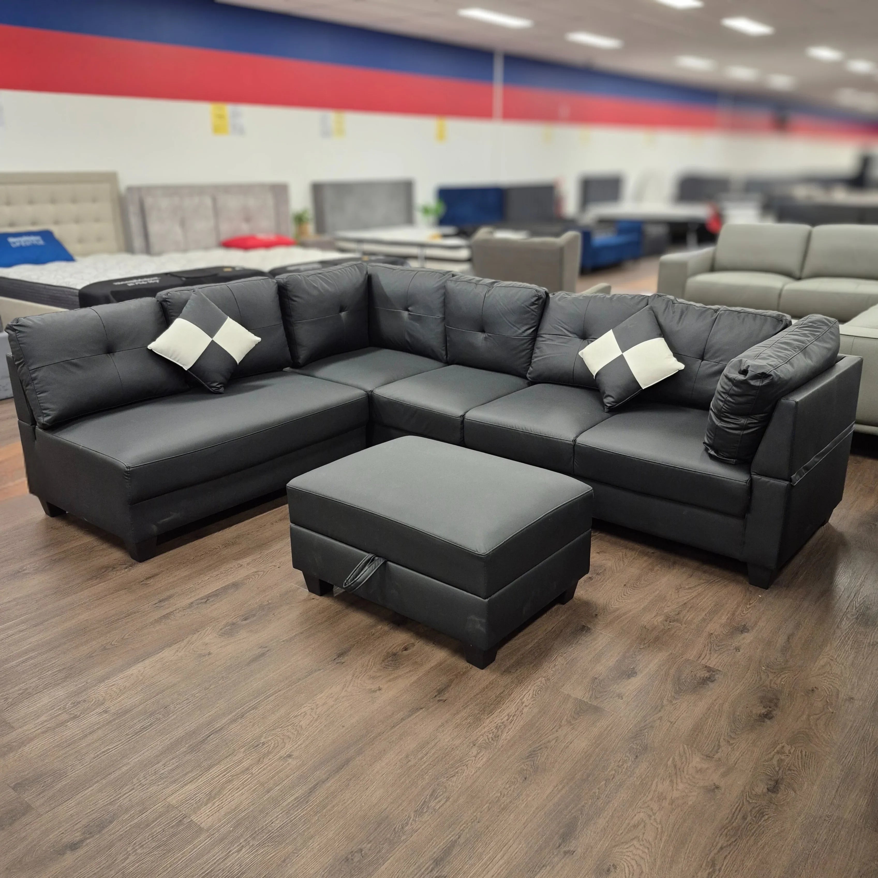 Black PU leather sectional sofa with matching ottoman and accent pillows in showroom