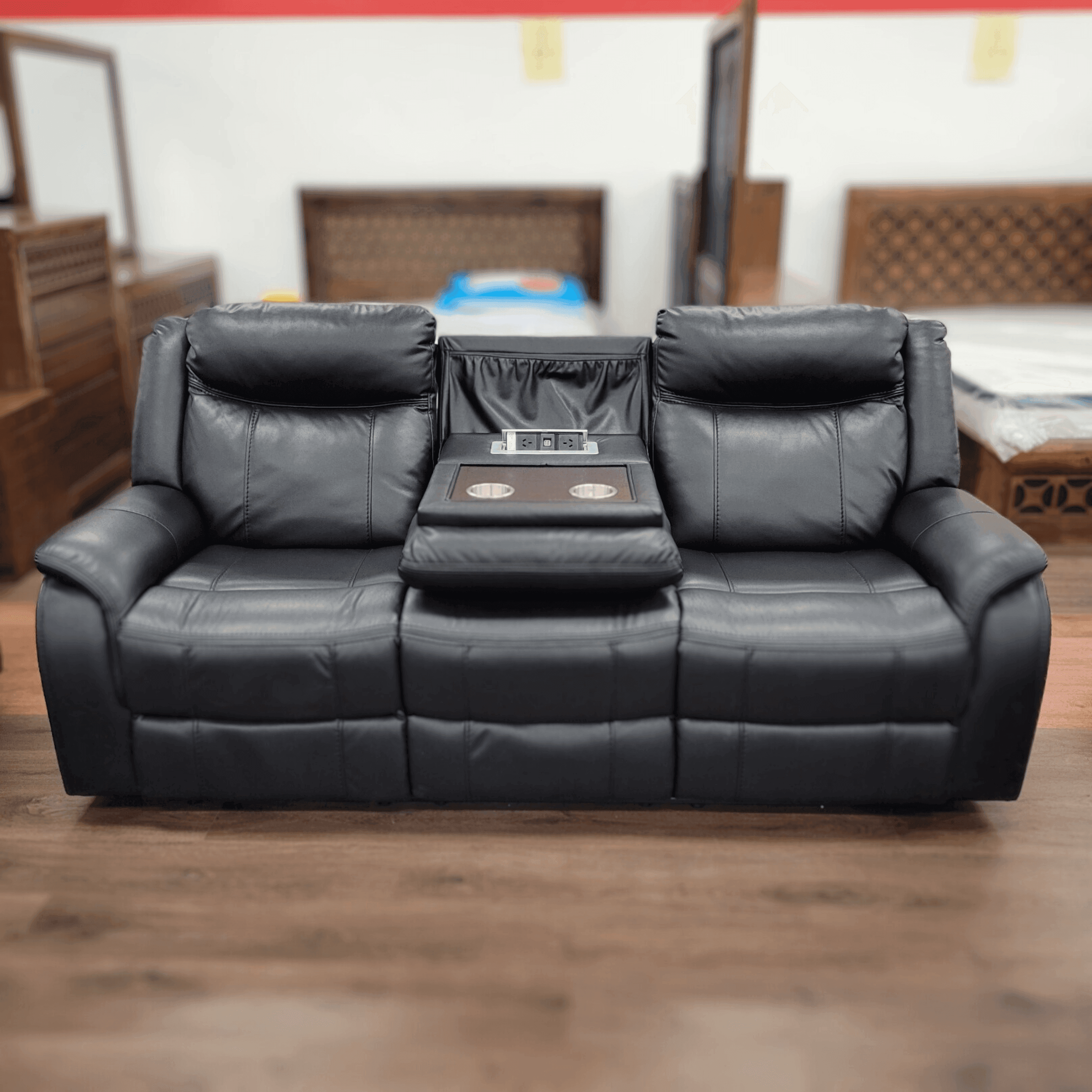 Black 3-seater recliner sofa with center console, cup holders, and USB ports in showroom