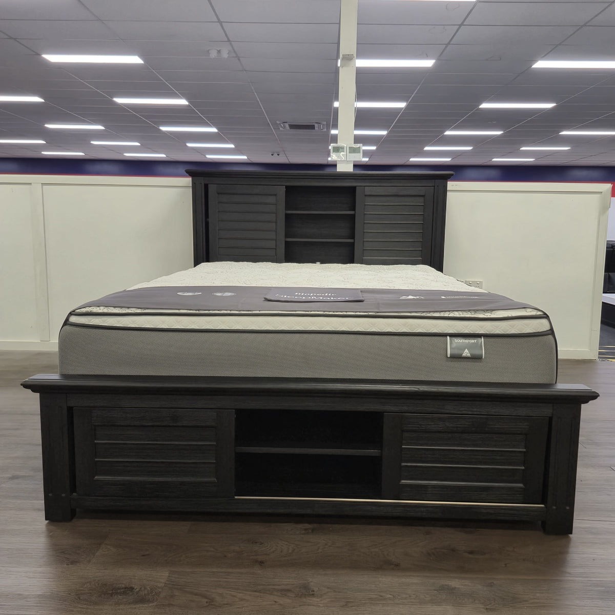 Warwick Bookcase Bed Frame in dark timber finish, full showroom view showing headboard bookcase shelving and footboard storage shelf, at The A2Z Furniture showroom. Mattress shown is not included.
