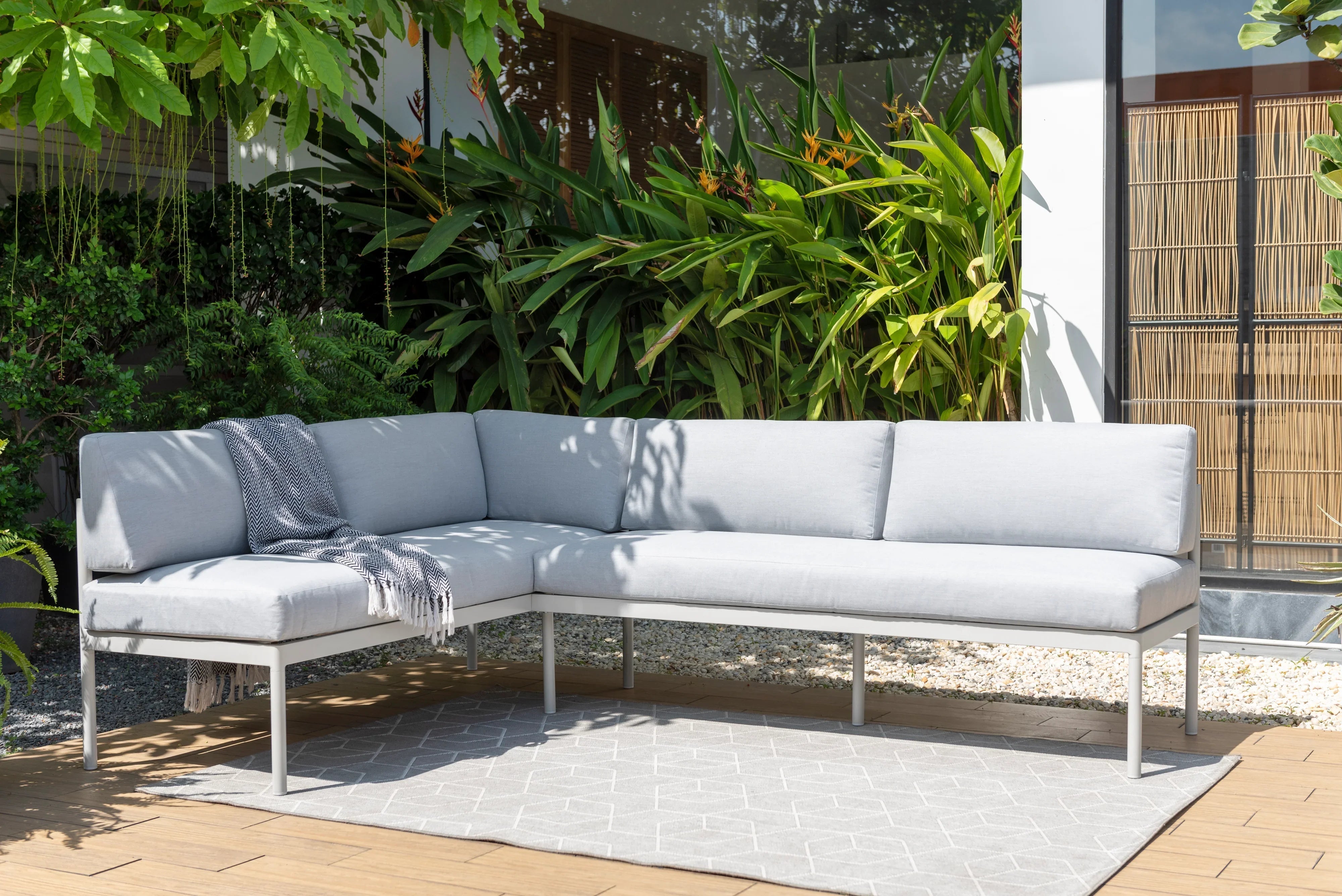 Modern light grey outdoor corner lounge set on patio with greenery and geometric rug