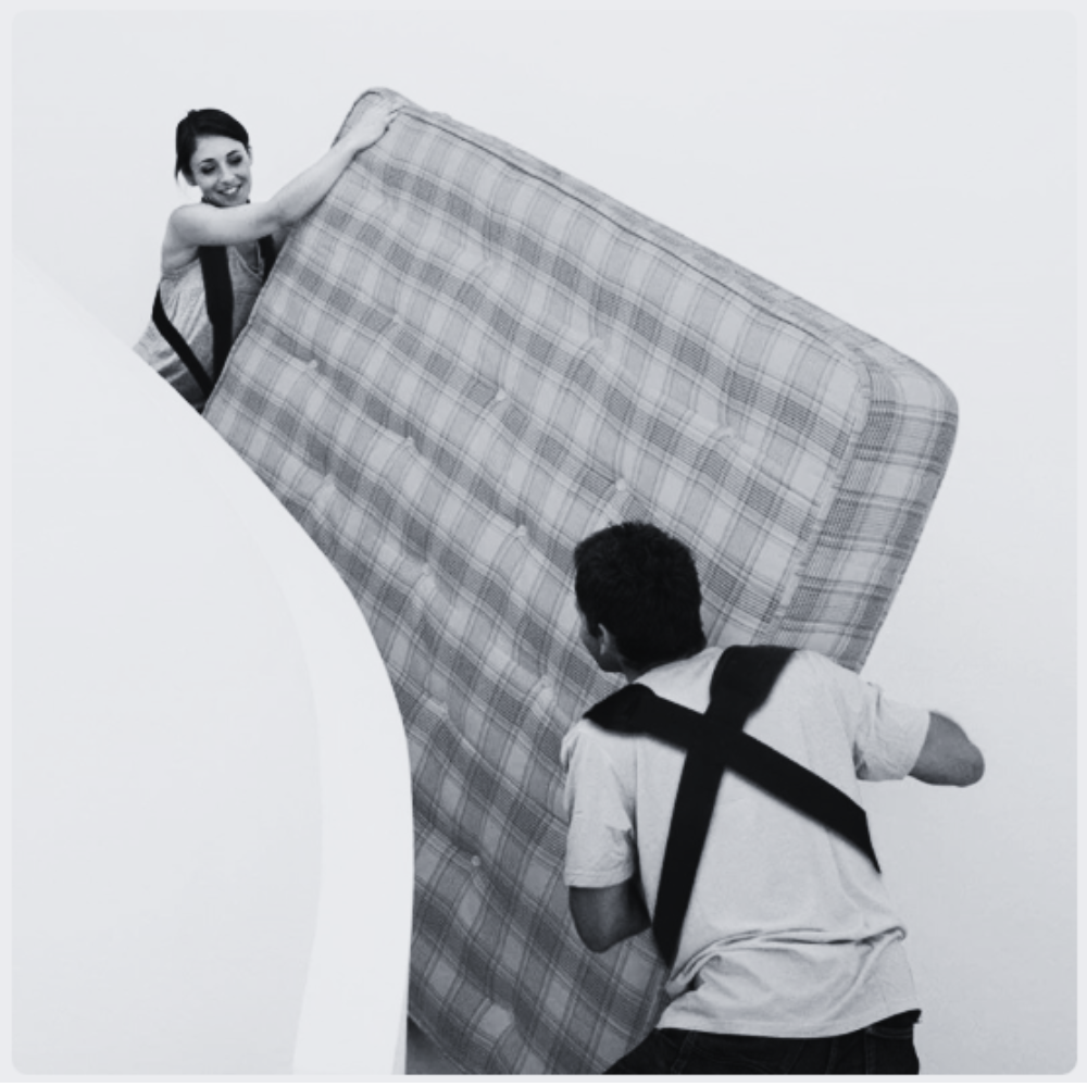 Two people carrying a mattress up a staircase using lifting straps.