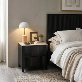 Caulfield bedside table in black with fluted ribbed drawer fronts and a stone-look top, styled beside a black fluted bed with a lamp - The A2Z Furniture