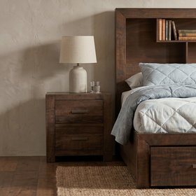 Sedona Bedside Table in rustic dark timber with two drawers and metal handles, topped with a lamp and water glass beside a bookcase bed - The A2Z Furniture