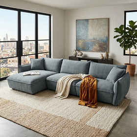 Gray sectional sofa in a modern living room with large windows and cityscape view.