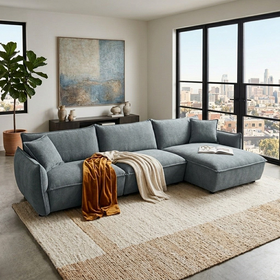 Opal L-shaped fabric lounge with chaise in blue-grey, draped with an orange throw in a modern apartment with city skyline view - The A2Z Furniture