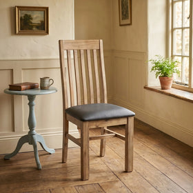 Wooden chair with a black cushion in a room with a small table and window.
