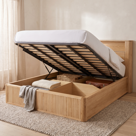 Canberra gas lift bed frame with the slatted mattress platform raised on its gas struts, showing the full-footprint storage cavity below holding a folded blanket, a woven basket and a suitcase - The A2Z Furniture