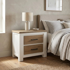 Wooden nightstand with lamp next to a bed in a bedroom setting