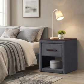 Gray upholstered nightstand next to a bed with pillows and a lamp in a bedroom setting.