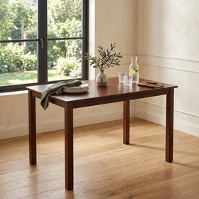 Wooden dining table with a vase, plates, and glasses in a room with large windows.