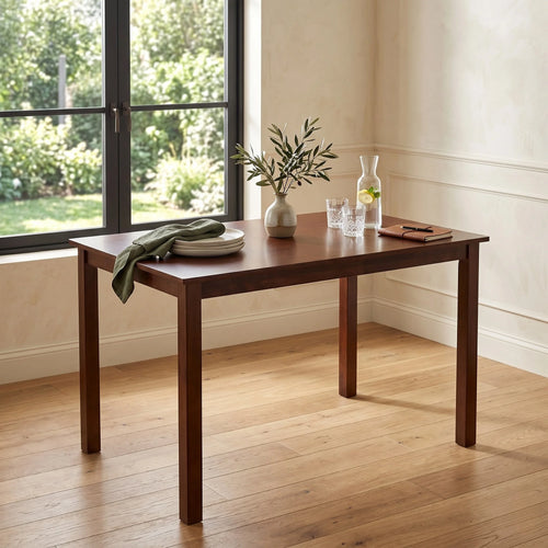 Wooden dining table with a vase, plates, and glasses in a room with large windows.