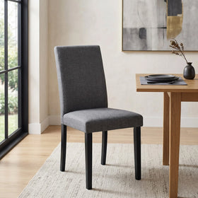Dixon Chair upholstered in charcoal grey fabric with black tapered legs, shown by a window beside a light oak dining table