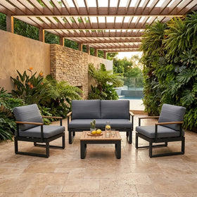 Outdoor patio set with gray cushions and a wooden coffee table in a garden setting.