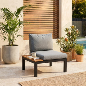 Outdoor patio chair with gray cushions and a small table, surrounded by potted plants.