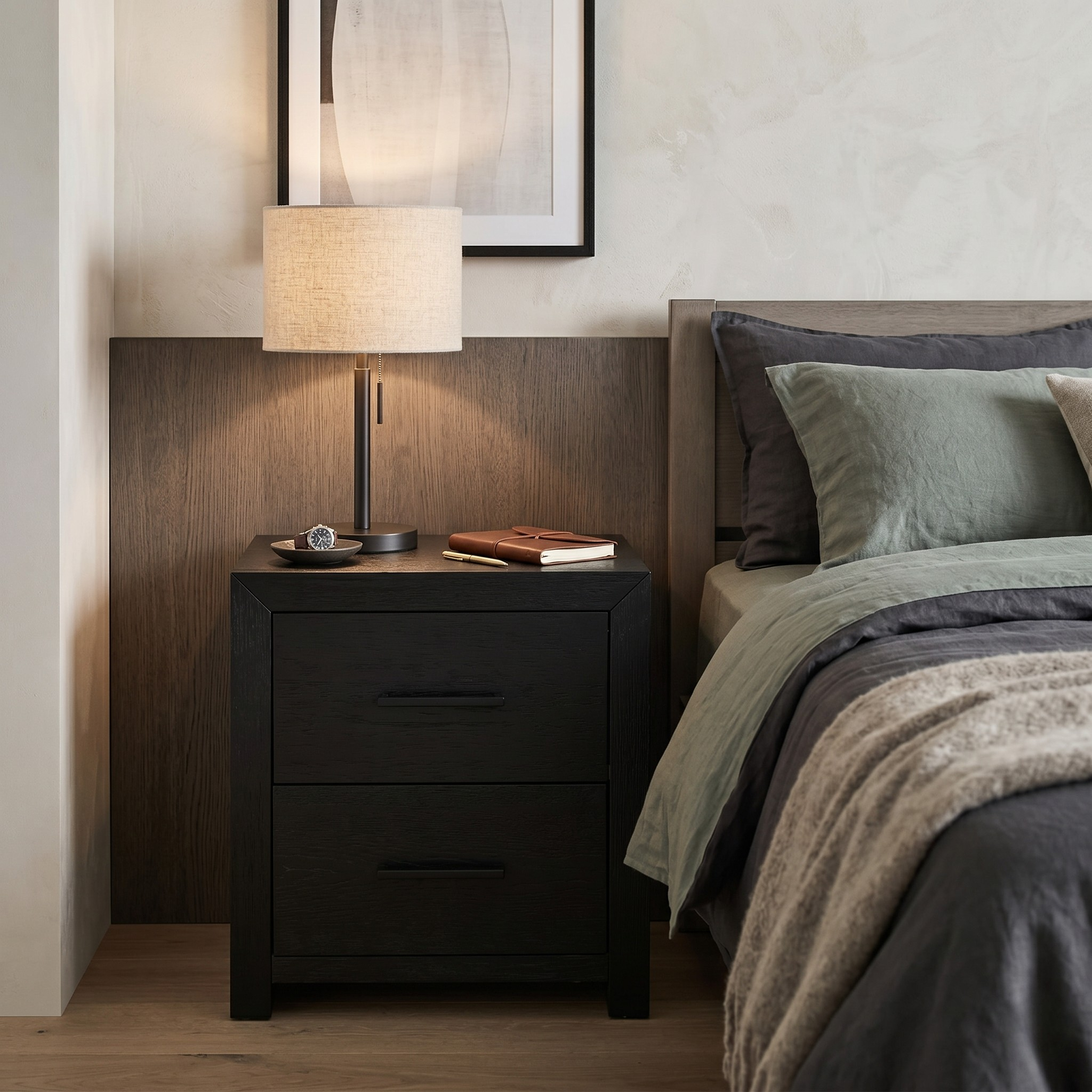 Bedroom with a nightstand featuring a lamp and books, next to a bed with green and brown bedding.