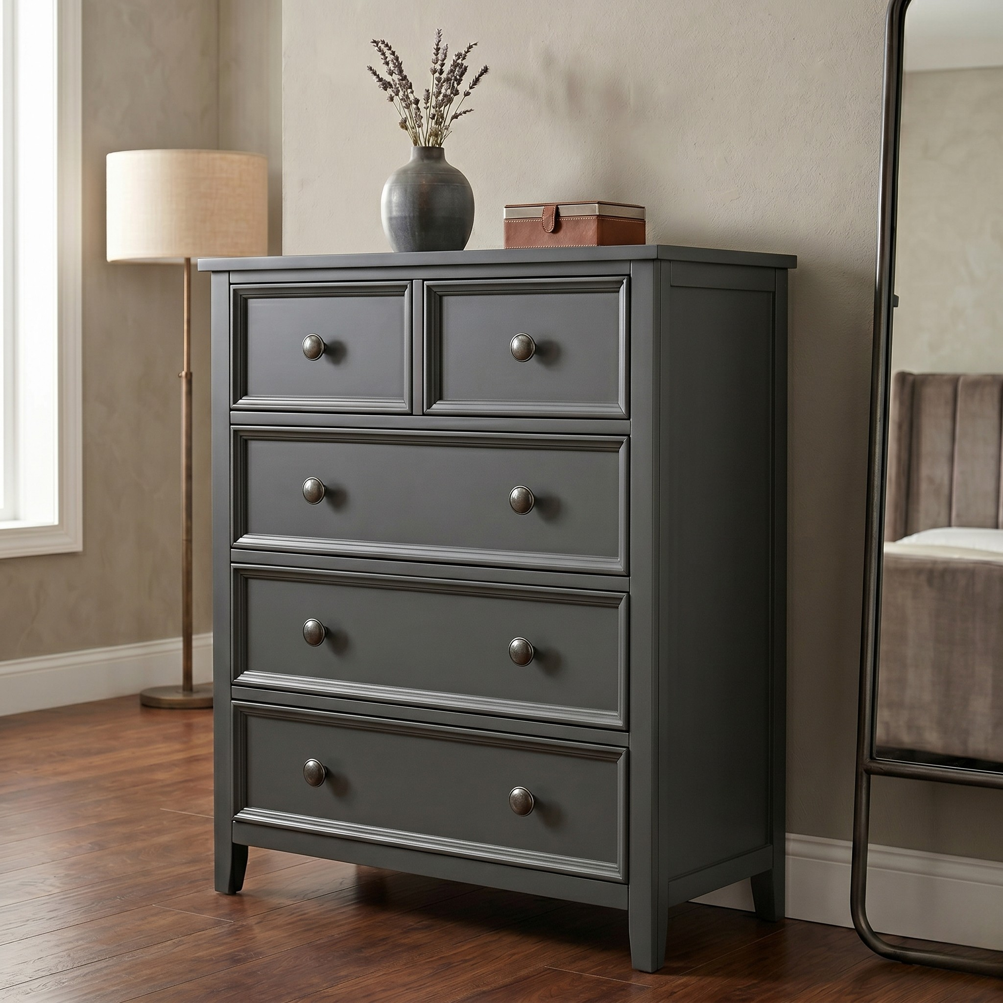 Gray dresser with four drawers in a room setting with a lamp and chair.