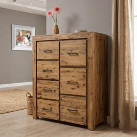 Wooden tallboy with multiple drawers in a room setting with a vase of flowers on top.