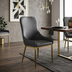 Dwayne Chair in black faux leather with slim brushed-gold metal legs, styled at a timber dining table against a textured grey wall
