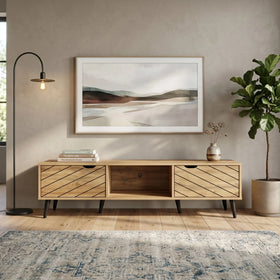 Wooden TV stand in a living room with a landscape painting above it, a plant to the right, and a rug on the floor.