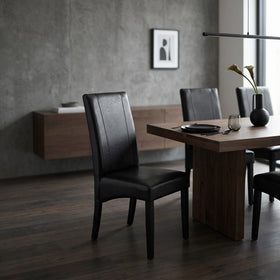 Dexter Chair black faux leather dining chair with a vertical stitched back panel and dark timber legs, beside a dark wood table