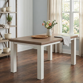 Wooden dining table with white base in a room with a window and shelves.