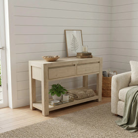 Light wood console table in a living room with decor items against a white paneled wall.