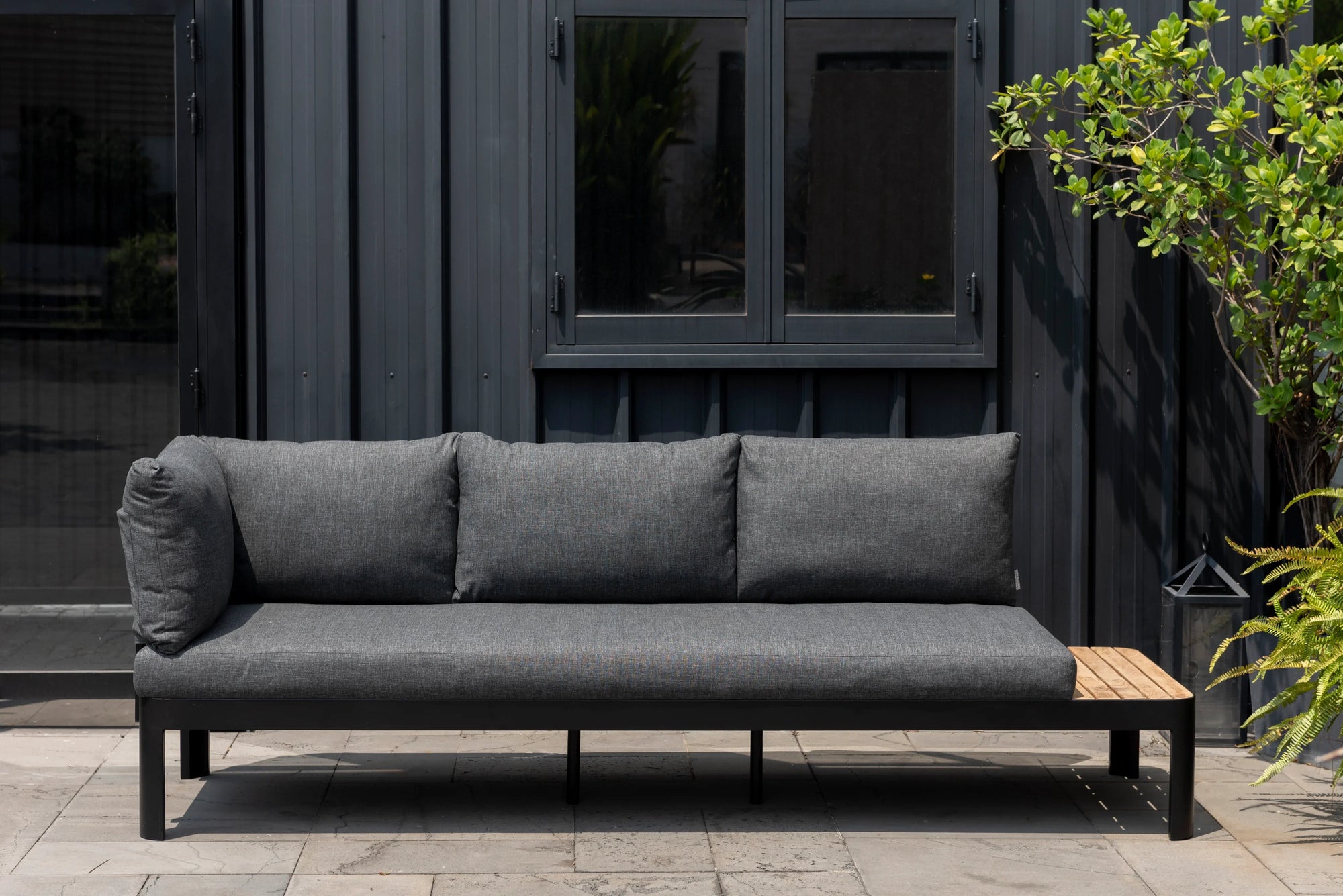 Modern tropical outdoor lounge with black aluminium frame, deep cushions and built-in teak side table for Queensland patios