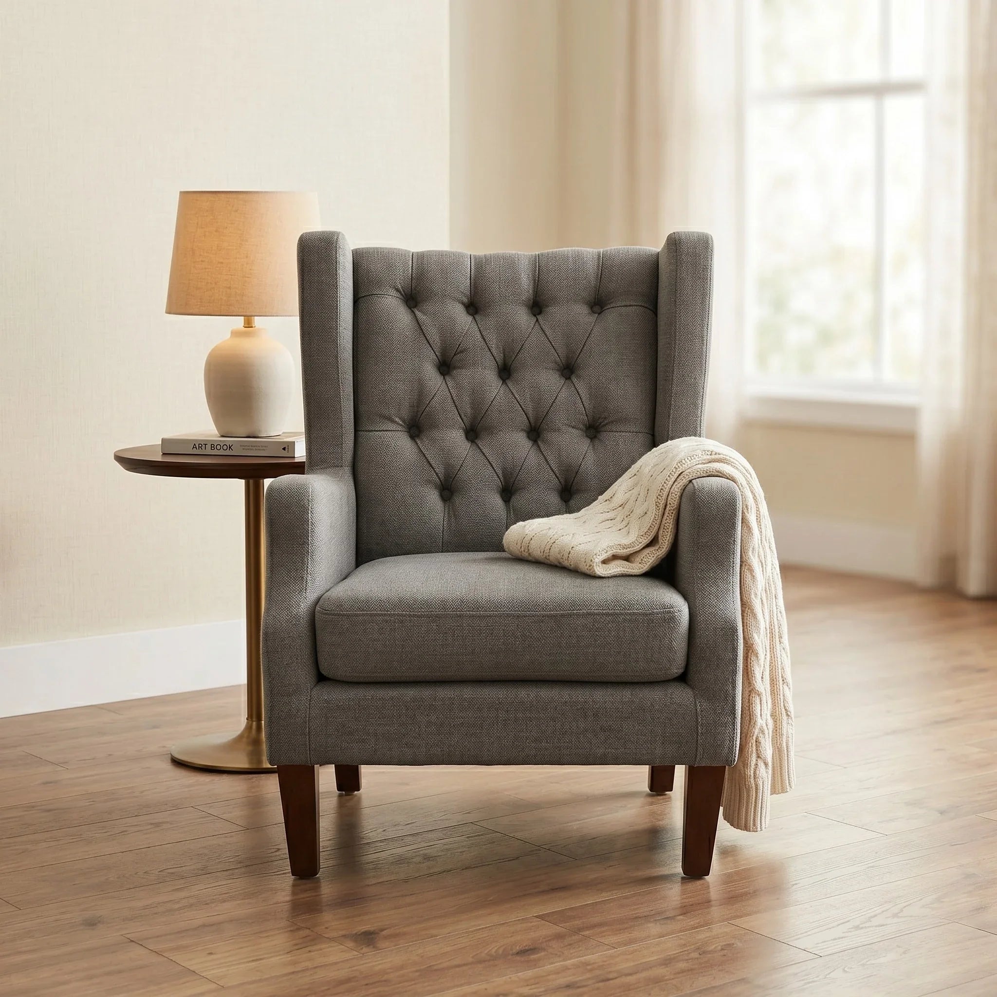 Maxwell Tufted Arm Chair in gray fabric with deep button tufting and wooden legs, styled with a cozy cream knit throw draped over one arm in a softly lit living room setting.