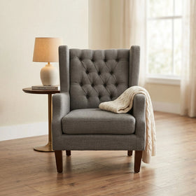 Maxwell Tufted Arm Chair in gray fabric with deep button tufting and wooden legs, styled with a cozy cream knit throw draped over one arm in a softly lit living room setting.