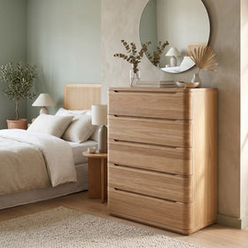 Canberra tallboy in natural oak with five curved-front drawers, styled beside a bed under a round mirror in a soft green bedroom - The A2Z Furniture