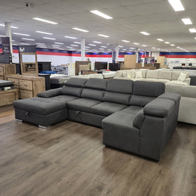 Alex Pull Out Sofa Bed in dark grey fabric, angled front-left view showing the full length of the lounge, in The A2Z Furniture showroom
