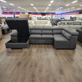 Alex Pull Out Sofa Bed in dark grey fabric with the chaise lid lifted on gas struts to show the empty storage compartment, in The A2Z Furniture showroom