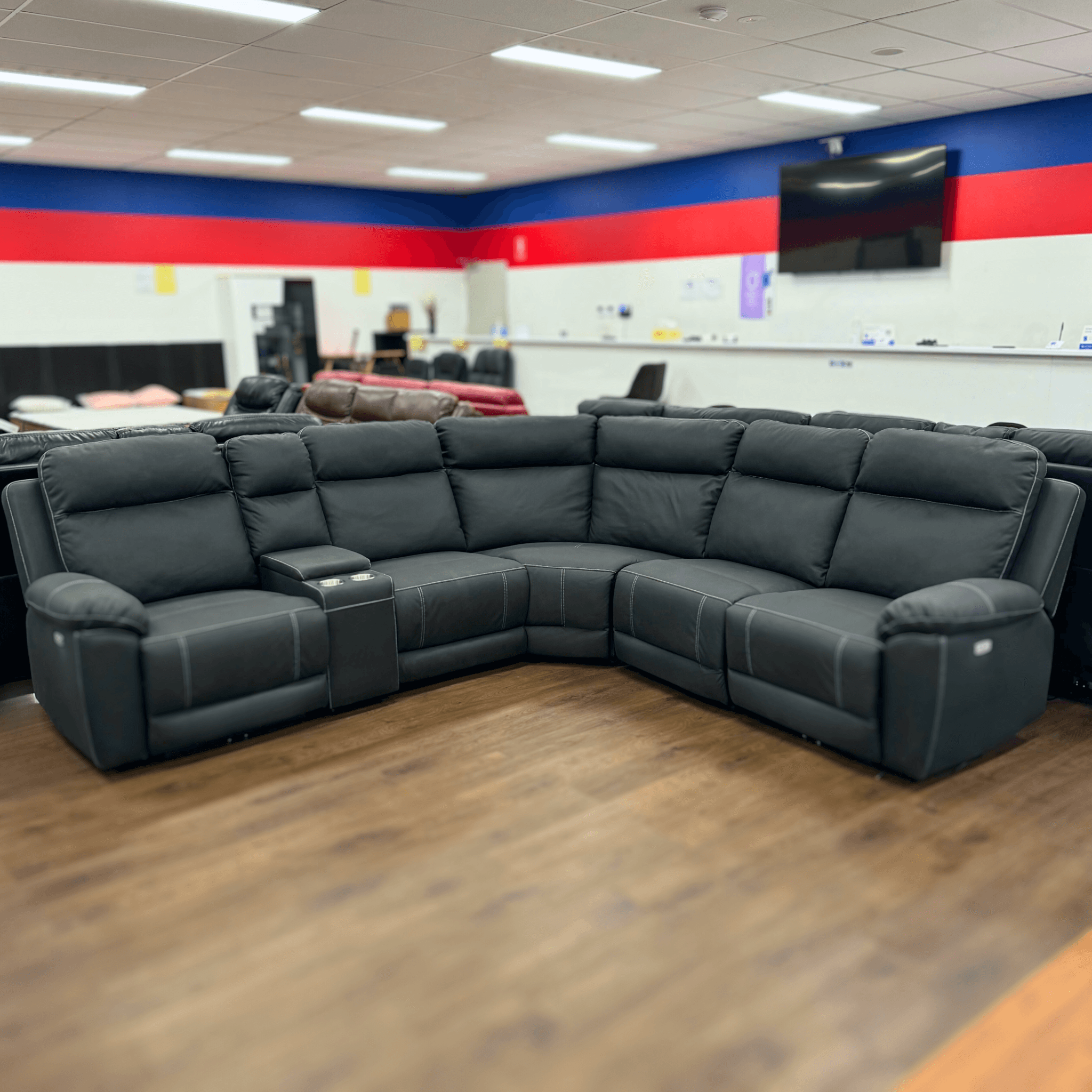 Black L-shaped recliner sectional sofa with cup holders in a showroom on wooden flooring