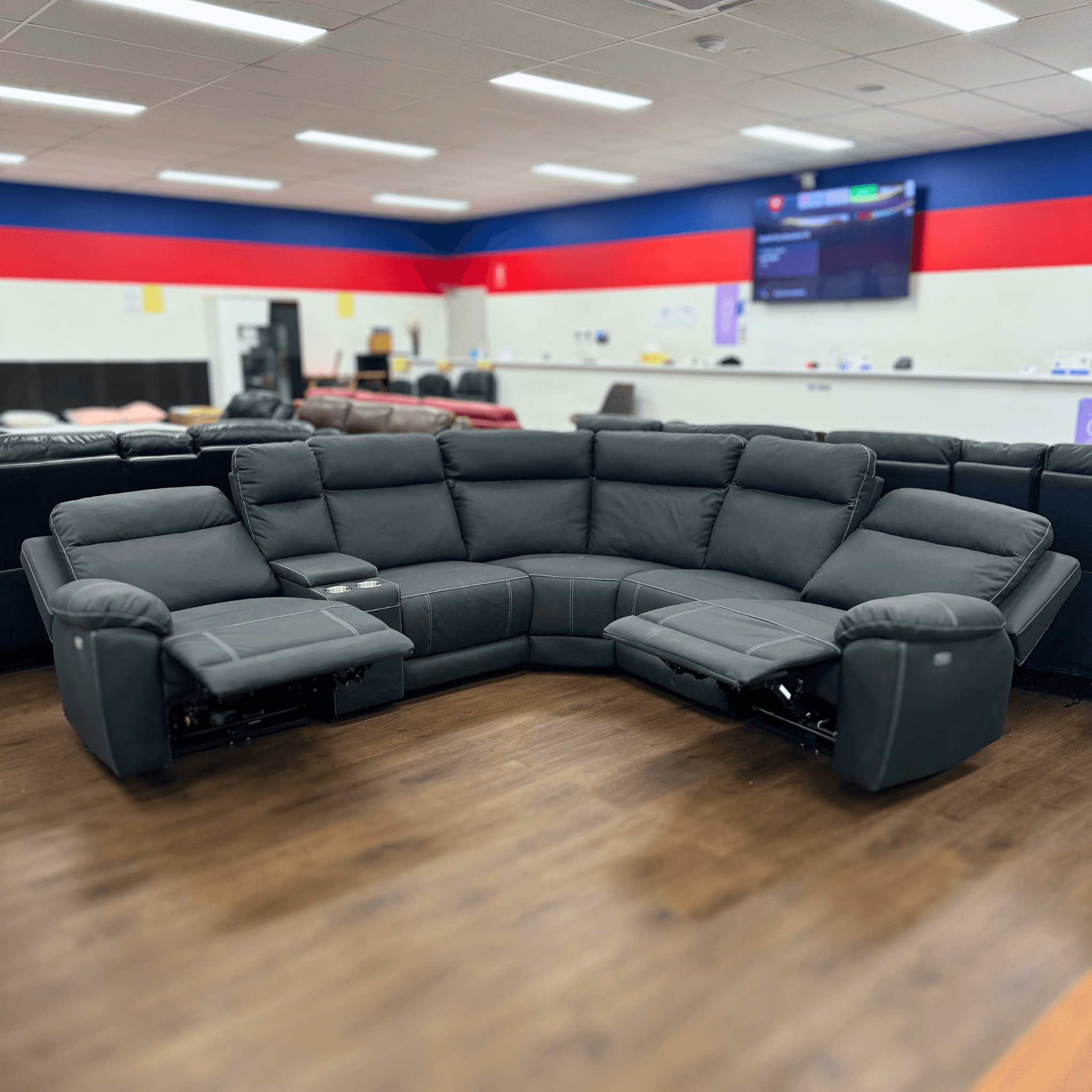 Black leather reclining sectional lounge suite with cup holders in a showroom setting