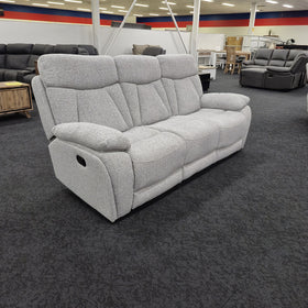 Baker 3 seater recliner lounge in light grey fabric viewed at an angle in The A2Z Furniture showroom, with the black manual recline pull handle visible on the outside arm