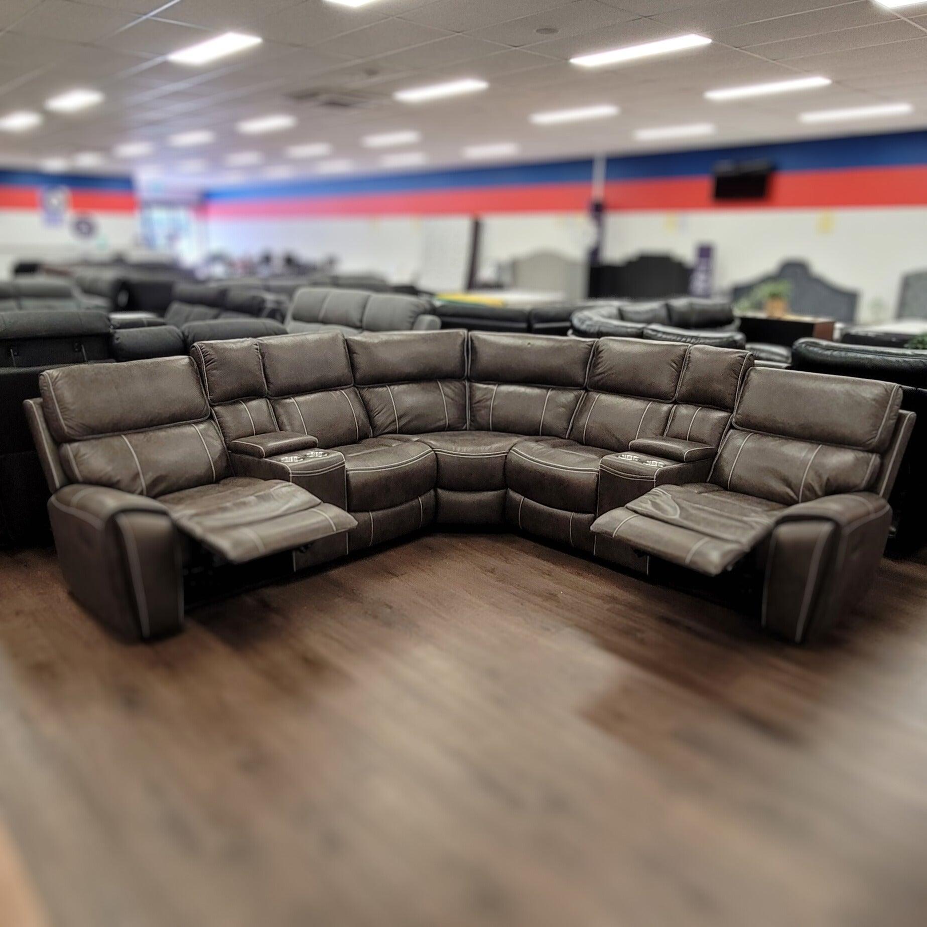 Modern brown leather recliner sectional sofa with cup holders in a furniture showroom