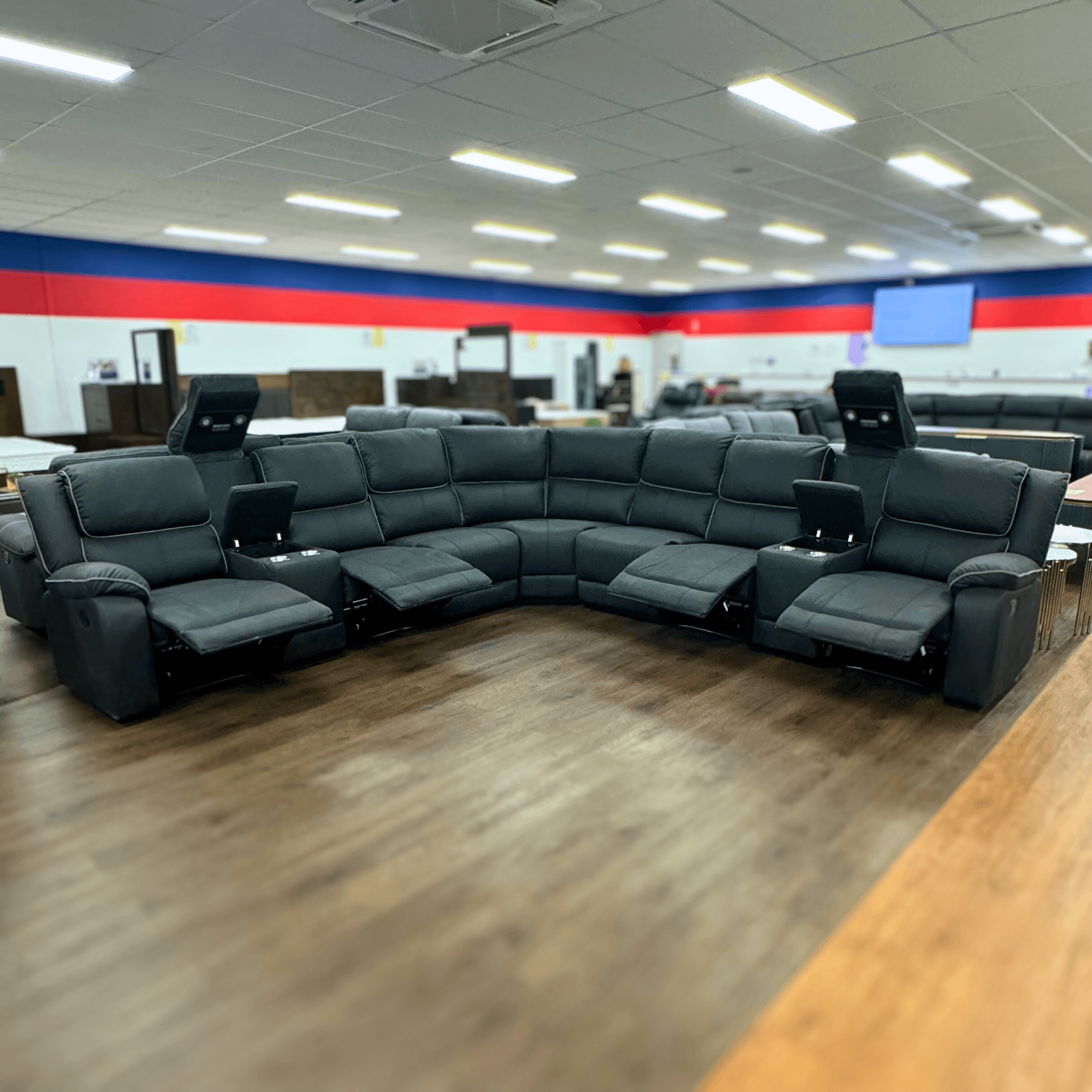 Black corner sectional recliner sofa with cup holders and open footrests in showroom