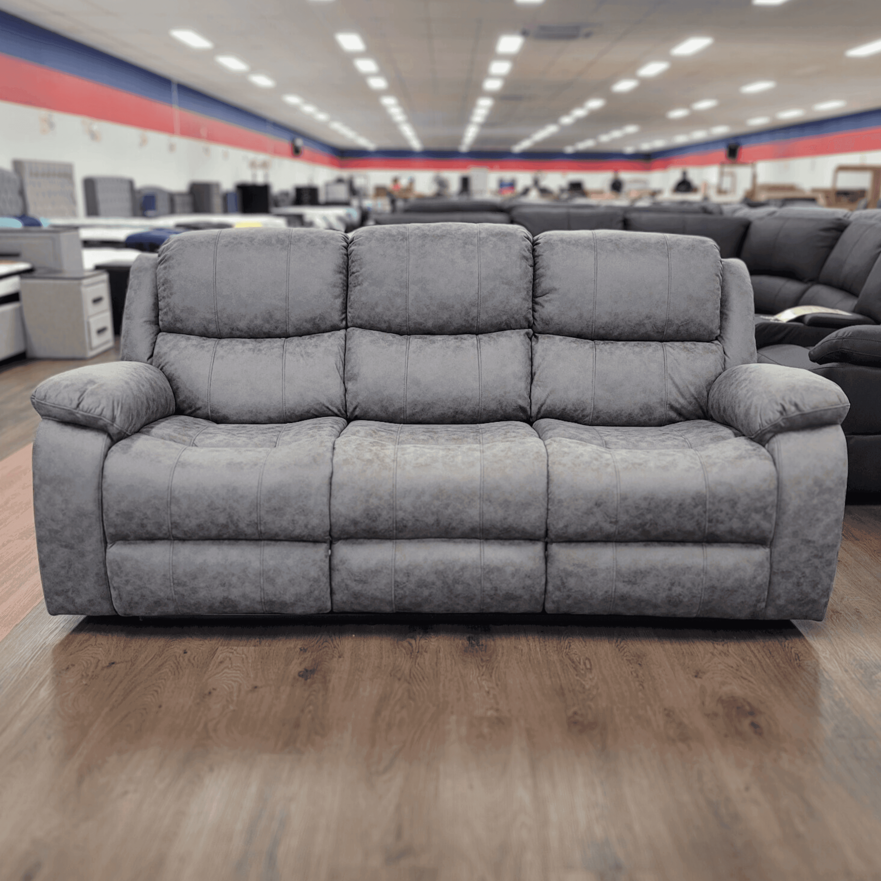 Modern grey fabric recliner sofa with plush cushions in a spacious furniture showroom
