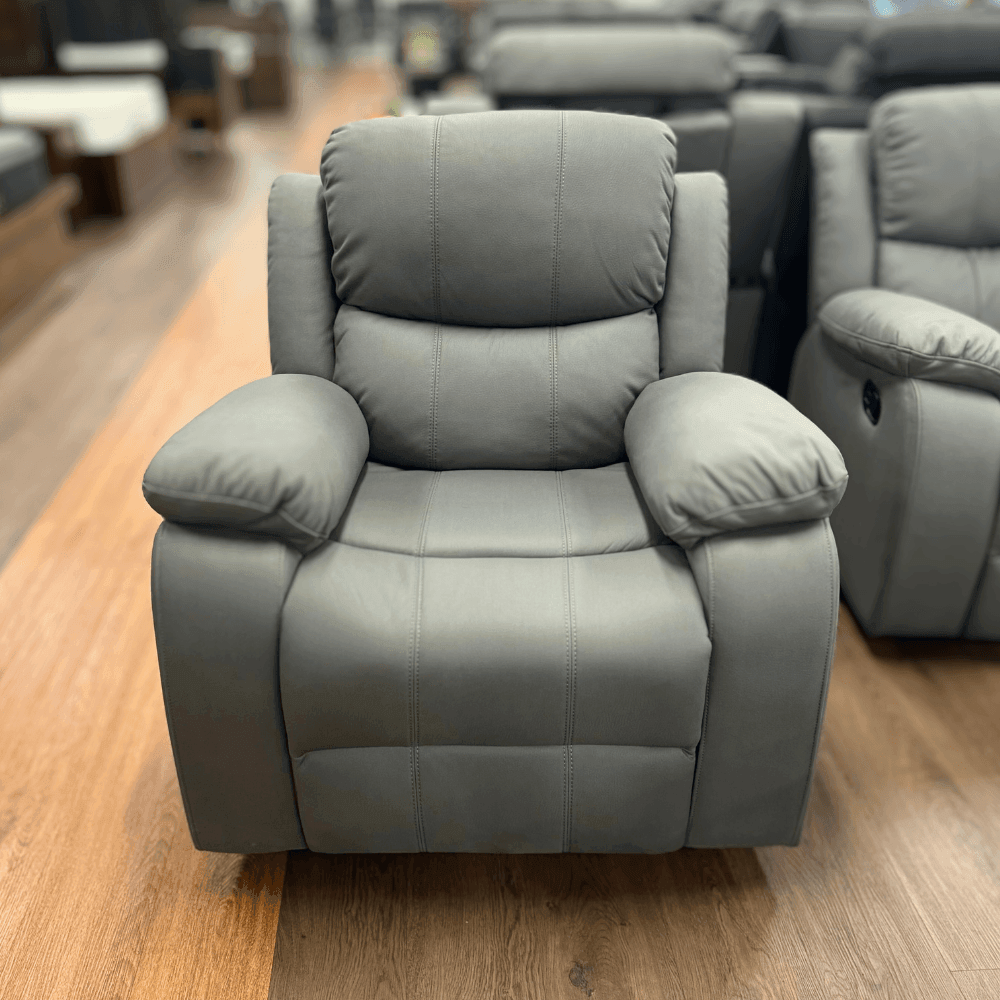 Grey recliner chair with padded cushions on a wood floor in a furniture showroom