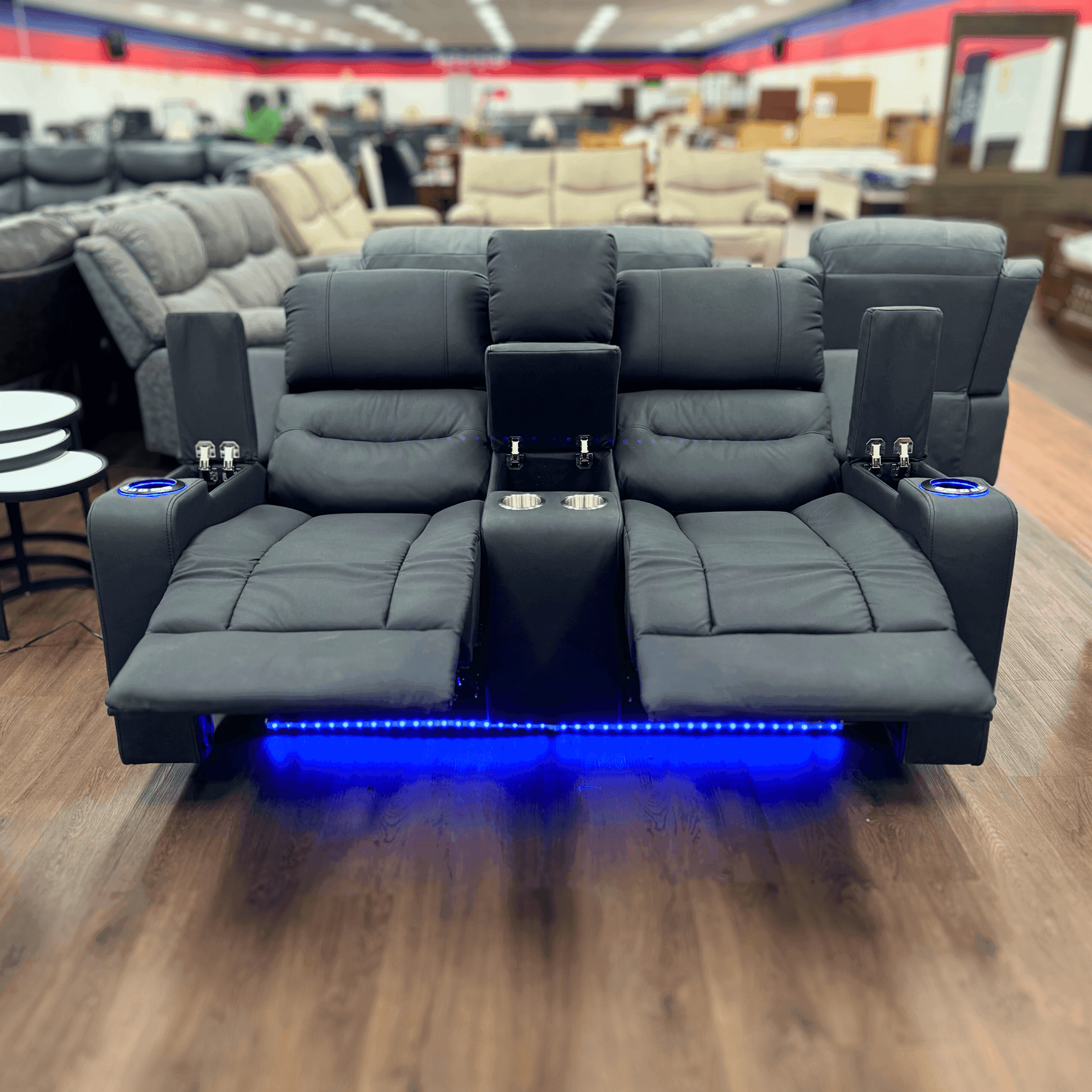 Black two seater recliner sofa with cup holders, storage, and blue LED lighting in a showroom