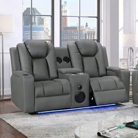 Breeze 2 Seater Dual Motor Electric Recliner Lounge in grey leather with built-in speakers and cup holders, set in a modern living room with cityscape windows.