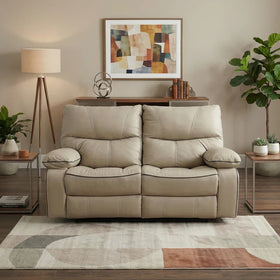 Brooke 2 Seater Recliner Lounge in beige leather with cushioned armrests and backrests, placed in a modern living room setting with abstract wall art, plants, and wooden furniture.