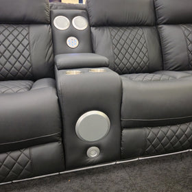 Bunbury black air leather corner recliner sofa - armrest console showing the twin overhead speakers, USB and AUX control panel, two stainless cupholders and the large front-facing speaker